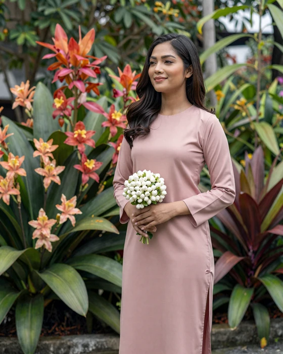 Graceful Malaysian woman in traditional baju kurung standing in a lush tropical garden