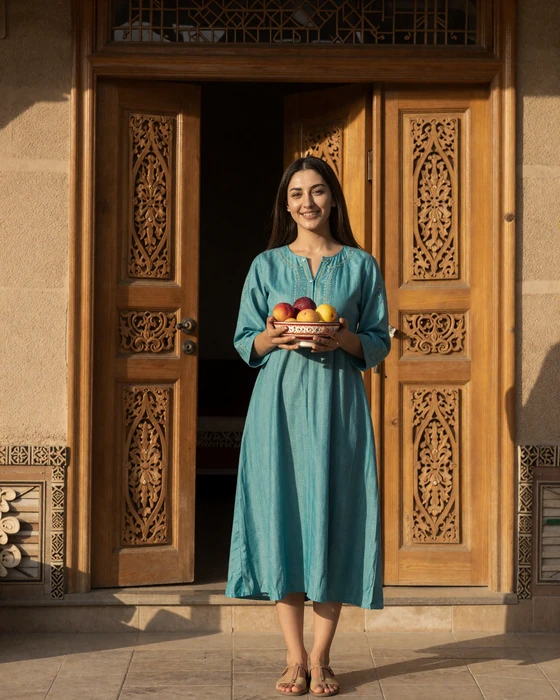 An Uzbek woman in traditional modern dress welcoming guests at a beautifully carved doorway