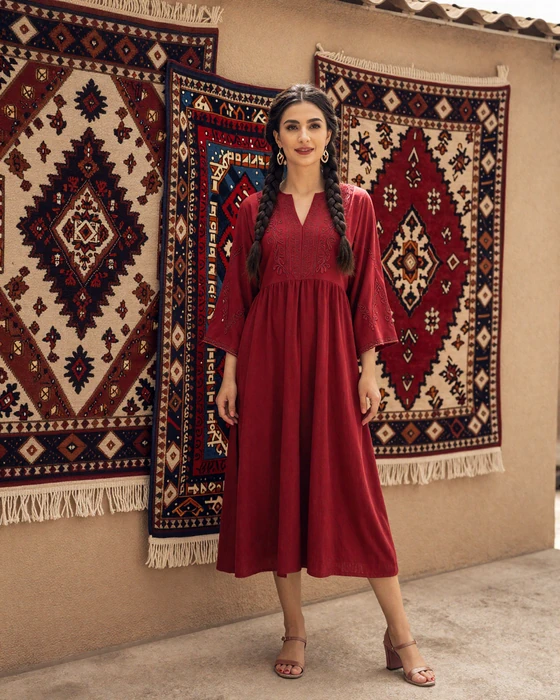 Turkmen woman in traditional embroidered dress standing near handwoven carpets in a sunlit courtyard